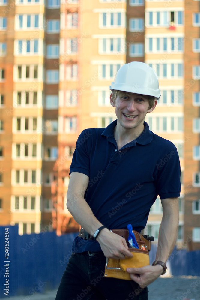 Smiling man in helmet stands at front of building construction Smiling man in helmet stands at front of building construction