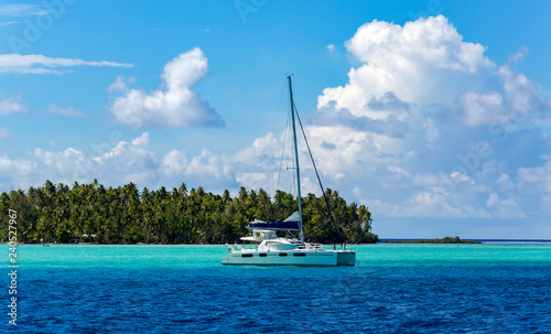 Photo Lonely catamaran in the turquoise lagoon on the background of the island of Tahaa in the Leeward group of the Society Islands of French Polynesia