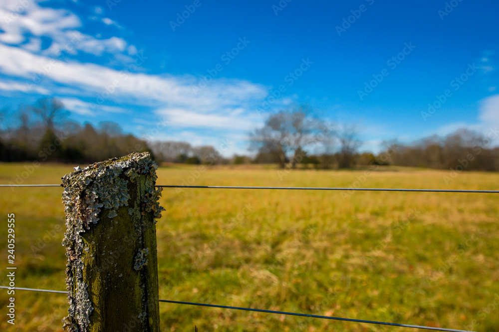 Fencepost with Wire Fence In Rural Country Field with blue skies in fall.