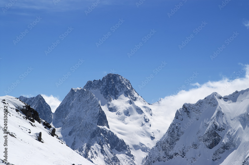 Winter snowy mountains in clouds and beautiful blue sky
