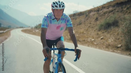 Motivated mature old man or senior is cycling or pedaling in a bicycle in countryside nature during a sunny autumn day enjoying a spot or hobby living a healthy long live wearing a helmet and form