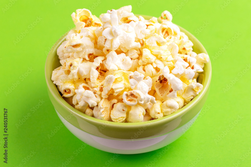 Tasty salty popcorn in bowl on bright green backgraund Tasty salty popcorn in bowl on bright green backgraund