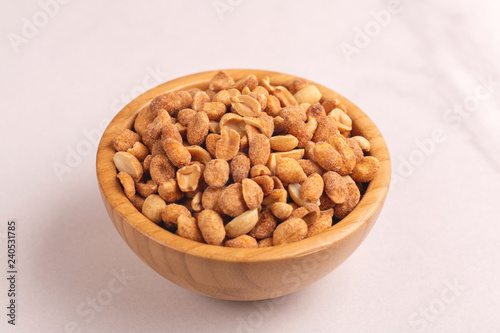 Roasted peanuts in wooden bowl on light marble background