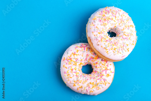 Two delicious vanilla donuts with sprinkle on bright blue background