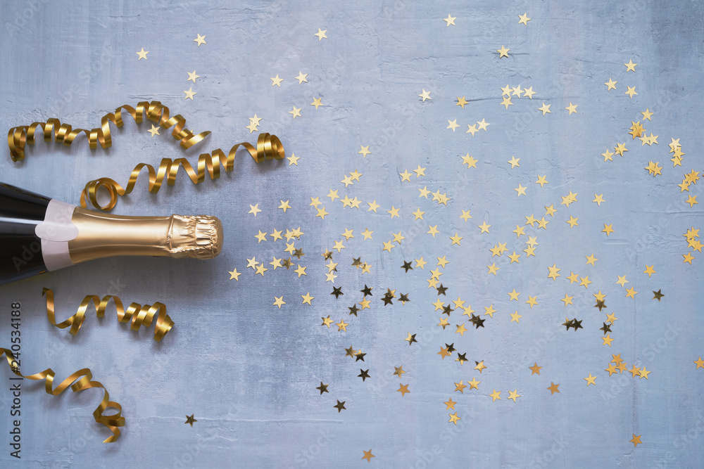 Champagne bottle with confetti stars and party streamers on blue background. Copy space,top view. Flat lay - obrazy, fototapety, plakaty 