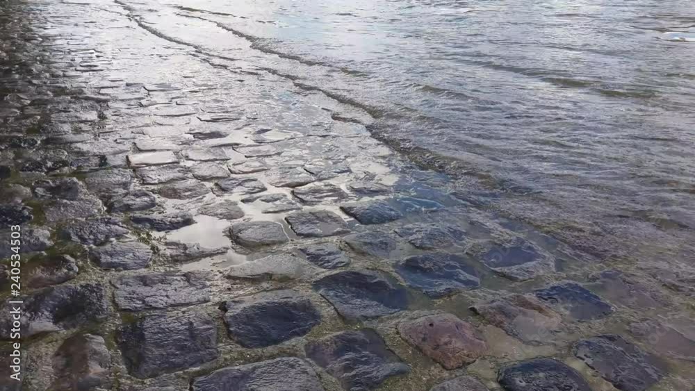 Footage of a river getting out on a cobblestone road in a city. Location: River Seine in Paris.