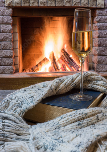 shampagne glass, opened book and wool scarf against cozy firepace. photo