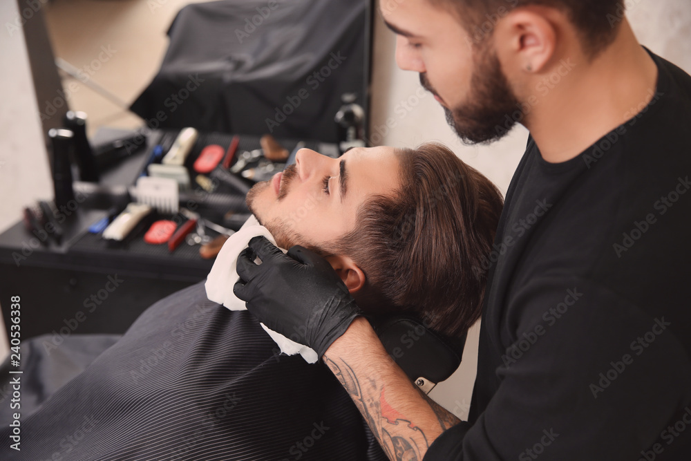Fototapeta premium Professional hairdresser using cold towel to calm client's skin after shaving in barbershop