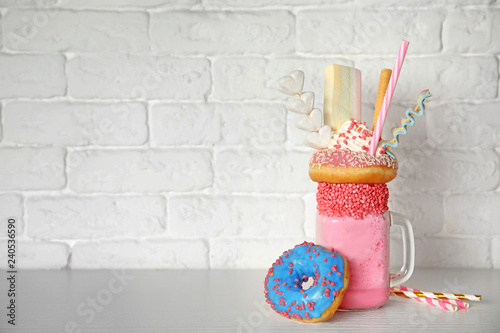 Mason jar of tasty milk shake with sweets on table near brick wall. Space for text