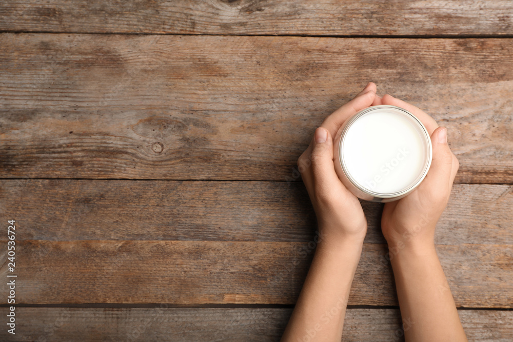 Woman holding glass of milk on wooden table, top view. Space for text Woman holding glass of milk on wooden table, top view. Space for text