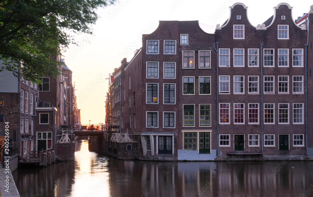 Sunset reflected in the water of the Amsterdam canal against the background of beautiful houses.
