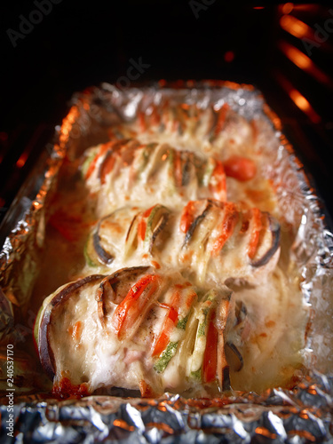 Baked in oven chiken fillet meat with tomato, eggplant and cheese. Roasted in oven chicken breasts coated with melted cheese. Food on a foil on glass pan in the oven. Healthy cooking