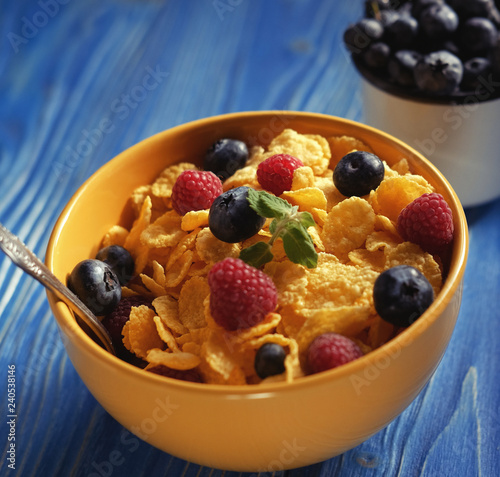 Cornflakes with berries raspberries and blueberries on blue wooden background.