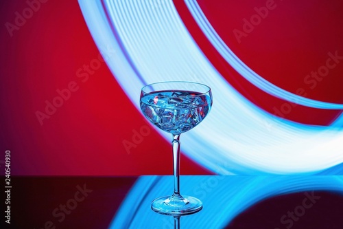 Beautiful view of alcohol drink with ice cubes in crystal glass on colorful background. 