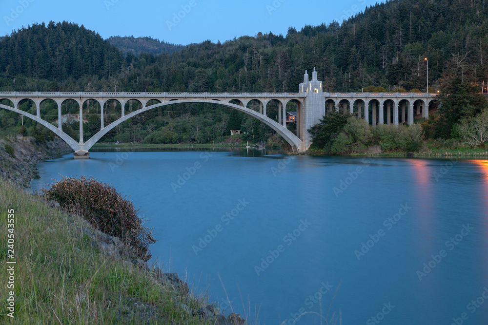 The Rogue River bridge with the obelisk illuminated at sunset in Gold Beach, Oregon, USA The Rogue River bridge with the obelisk illuminated at sunset in Gold Beach, Oregon, USA