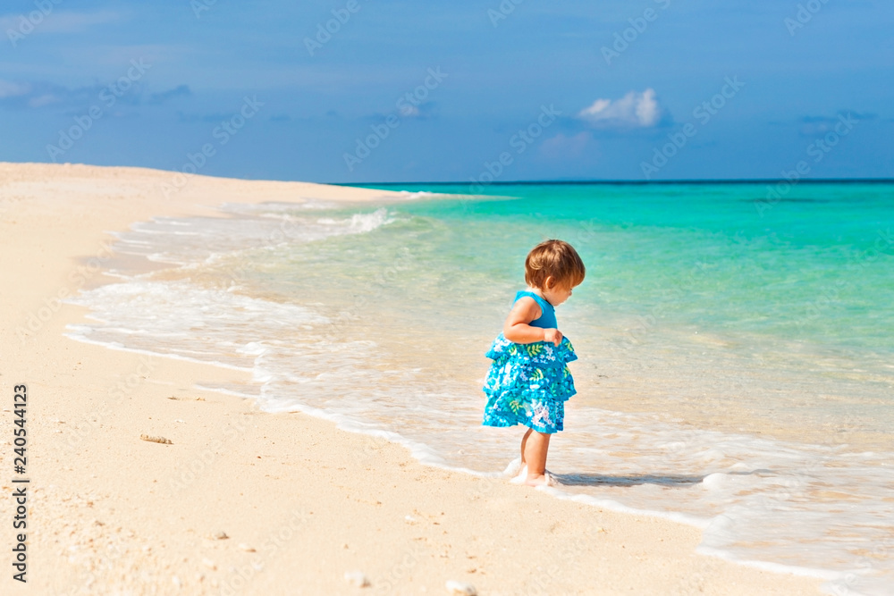 Cute baby in blue dress walking on the beach with white sand on the shore of the turquoise ocean. Boracay. Philippines