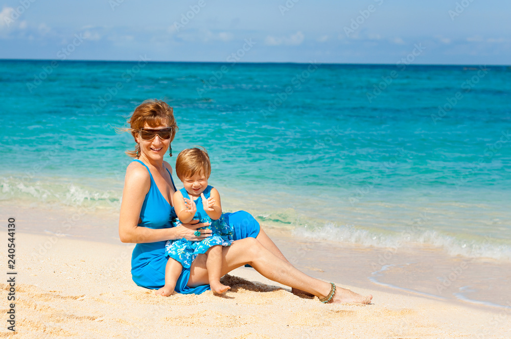 Mother with her Cute baby in blue dress having fun on the white sand beach on the shore of the turquoise ocean. Boracay. Philippines. Family vacation