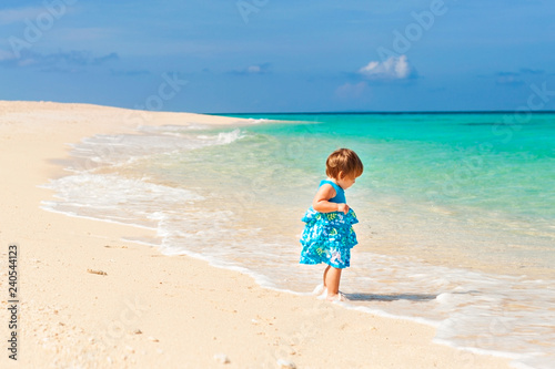 Cute baby in blue dress walking on the beach with white sand on the shore of the turquoise ocean. Boracay. Philippines