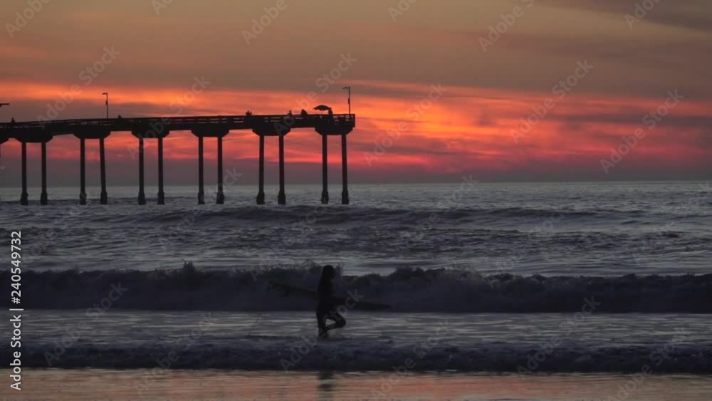 surfer walks at the beach with surfboard as silhouette in slow motion