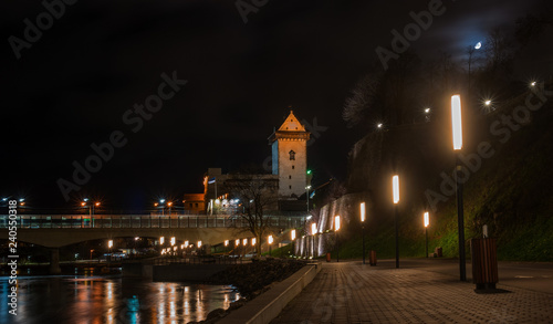 Night view of Narva castle with the tower of High Herman, Narva, Estonia. The castle is illuminated. In the foreground is the city promenade. Opposite Narva is the Russian city of Ivangorod