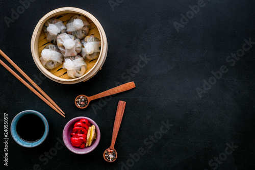 Dim sums with red pepper and vegetables with sticks and black tea in Chinese restaurant on black background top view mockup © 9dreamstudio