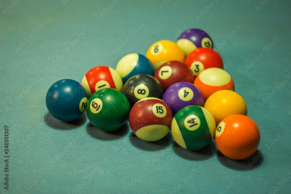 blurred multi-colored billiard balls lie in the shape of a triangular pyramid on the blue cloth of the table blurred multi-colored billiard balls lie in the shape of a triangular pyramid on the blue cloth of the table