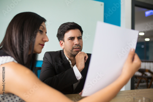 Young female secretary showing document to puzzled executive. Businesswoman showing data on paper to male colleague at meeting. Planning and teamwork concept