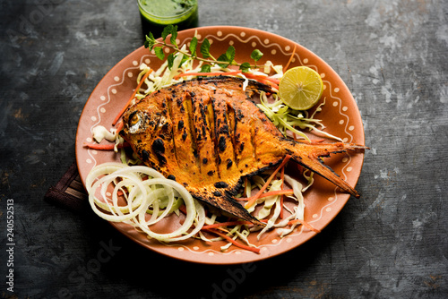 Foto Tandoori Pomfret fish cooked in a clay oven and garnished with lemon , mint, cabbage and carrot salad