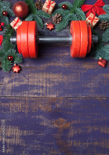 Christmas or New Year on a violet wooden background. Composition with dumbbells, gift, red and gold glass balls, fir tree branches for healthy lifestyle and sport