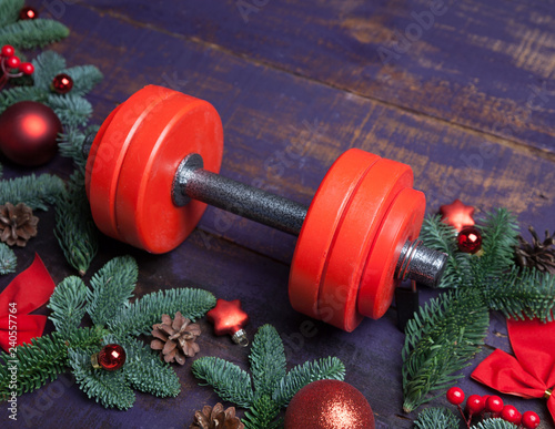 Christmas or New Year on a violet wooden background. Composition with dumbbells, gift, red and gold glass balls, fir tree branches for healthy lifestyle and sport