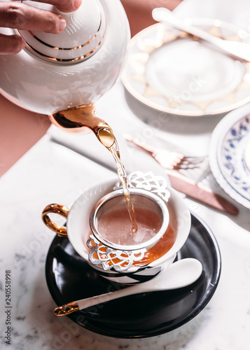 Hot Apple Tea served by pouring from mug through stainless steel tea strainer infuser in porcelain vintage cup.