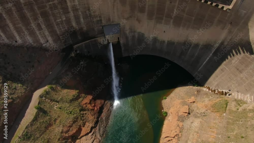 Aerial view of Katse hydroelectric Dam in Lesotho between mountains on a sunny day, moving backwards and tilting up to reveal landscape surrounding the dam wall.