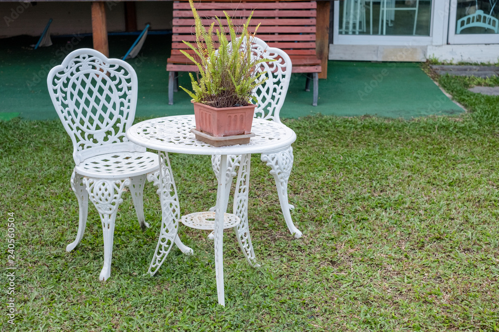 White vintage table and chairs with fern plant in vase on lawn
