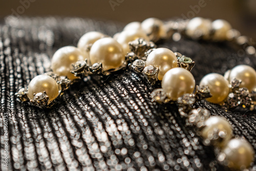 Women's metal jewelry made of pearls. Silver accessory for girls on a silver fabric background, texture. White and milk pearl products with transparent stones and rhinestones.