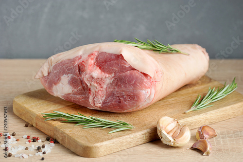 Uncooked pork knuckle on a wooden tray. Rosemary, garlic, salt and pepper for pickling shank. Light gray background. Close-up.