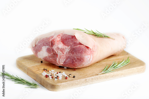 Uncooked pork knuckle on a wooden tray. Rosemary, salt and pepper for pickling shank. White background. Close-up.