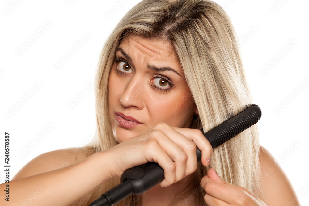 nervous young woman ironing her hair with hair iron on white backgrund nervous young woman ironing her hair with hair iron on white backgrund