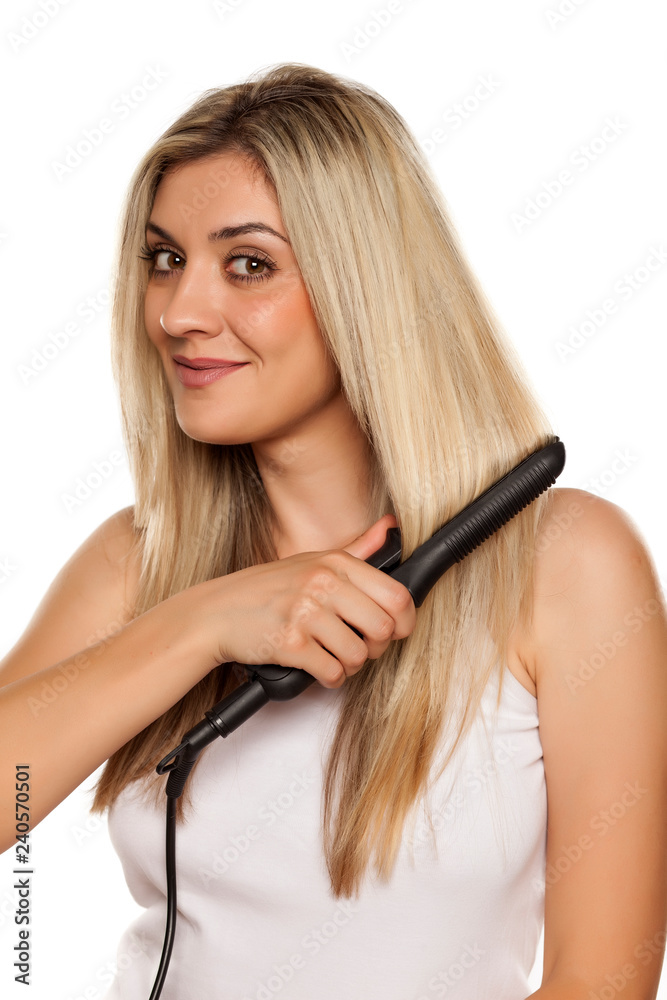 smiling young woman ironing her hair with hair iron on white backgrund smiling young woman ironing her hair with hair iron on white backgrund