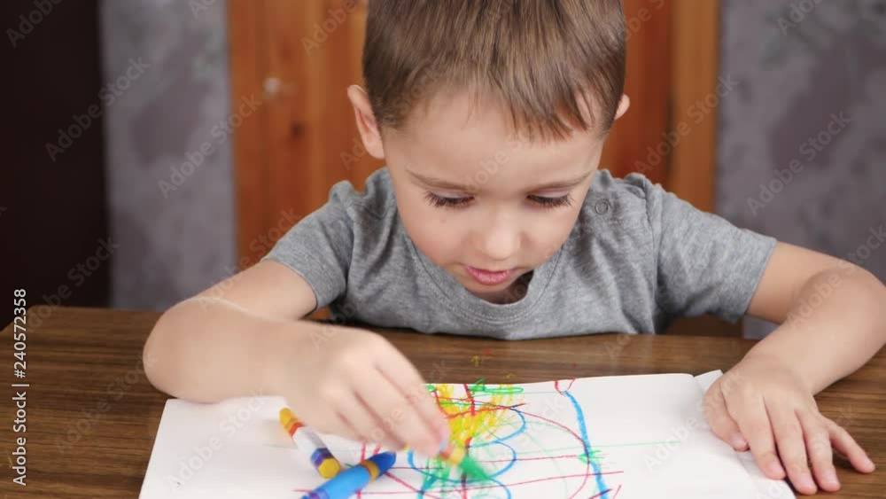Unknown child draws with bright pencils while sitting at the table. Development and education of children of preschool age. Unknown child draws with bright pencils while sitting at the table. Development and education of children of preschool age.