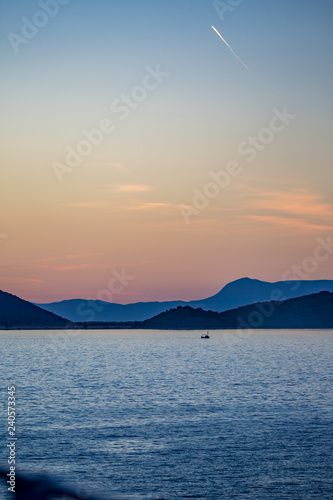 Scenery sunset seascape in Ionian Sea with mountain range far away and the silhouette of small fishing boat, picture taken in the golden hour