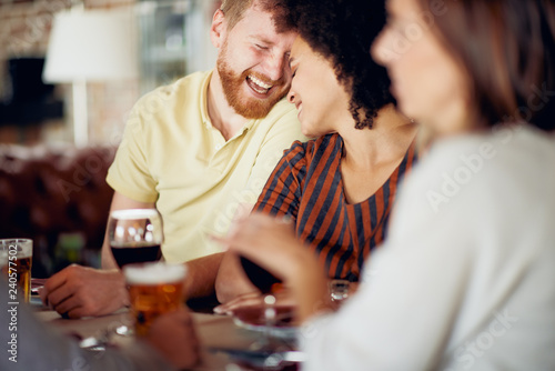 Friends chatting and drinking alcohol while  sitting at restaurant. Multi ethnic group.