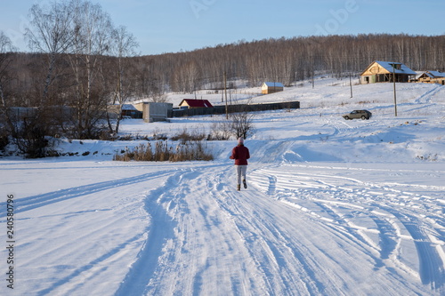 The girl runs away over the frozen lake in the direction of the village on a hill, on a winter sunny day.