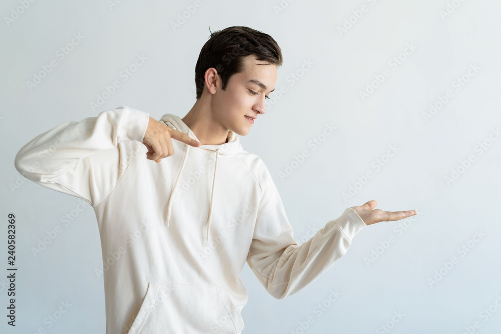 Content teen boy holding empty space on palm and pointing at it. Handsome young guy advertising product. Recommendation concept. Isolated view on white background. Content teen boy holding empty space on palm and pointing at it. Handsome young guy advertising product. Recommendation concept. Isolated view on white background.