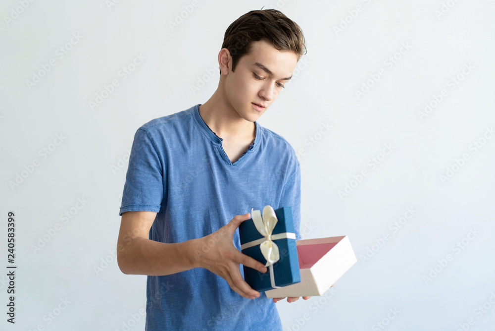 Serious teen boy holding open gift box. Young man standing and looking into gift box. Gift concept. Isolated view on white background. Serious teen boy holding open gift box. Young man standing and looking into gift box. Gift concept. Isolated view on white background.