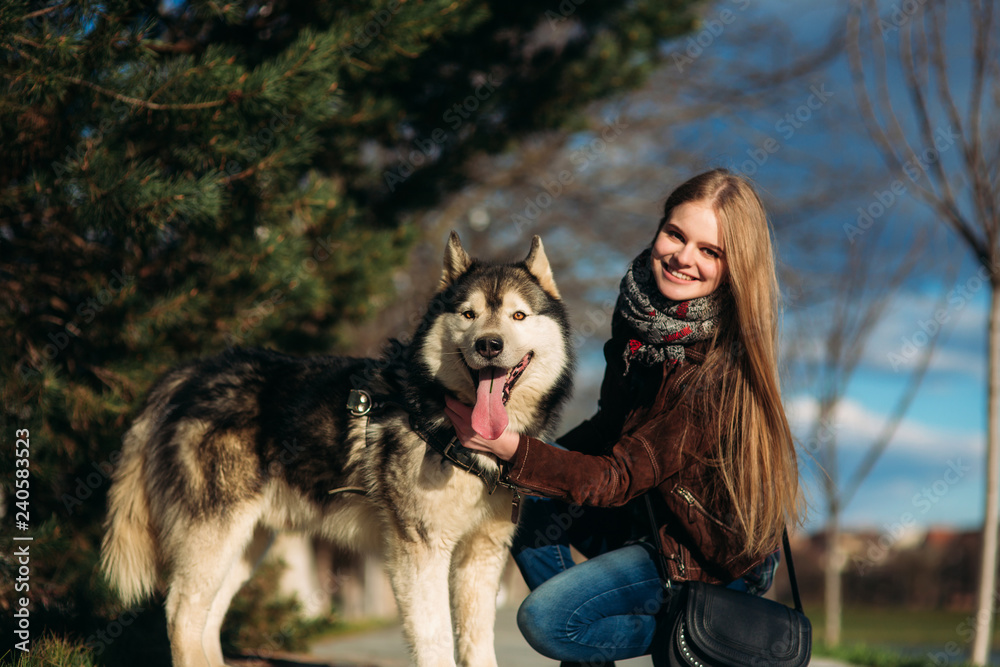 A smiling girl is walking with a dog along the embankment. Beautiful husky dog A smiling girl is walking with a dog along the embankment. Beautiful husky dog
