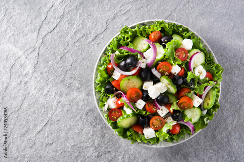 Fresh Greek salad in Plate with black olive,tomato,feta cheese, cucumber and onion on gray background. Top view. Copyspace