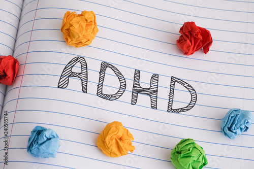 Abbreviation ADHD on notebook sheet with some colorful crumpled paper balls on it