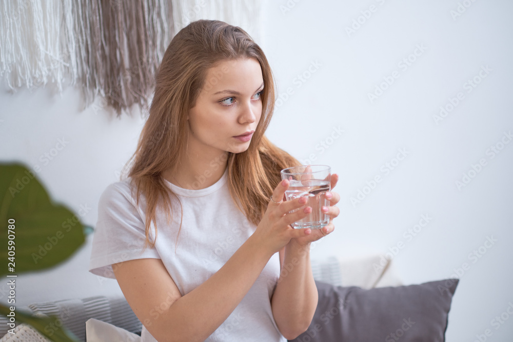 woman drinking water in the morning at home. detox concept, health care. blonde in a white T-shirt in a cozy room. woman drinking water in the morning at home. detox concept, health care. blonde in a white T-shirt in a cozy room.