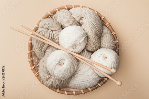 top view of yarn and knitting needles in wicker basket on beige background