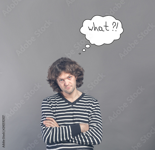 Skeptical man looking suspicious and questionable with drawn cloud of thoughts with what question in it. Some disapproval on his face on gray background. Human emotions, facial expressions, feelings photo